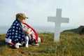 A young boy in a military cap, covered by the flag of the united states sitting on the grave of his deceased father. May 27th