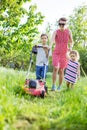 Young boy mowing grass with lawn mower, his mother and sister encouraging him Royalty Free Stock Photo