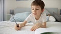 Young boy in pajamas writing in a notebook while lying in bed, doing his homework. Education and child development in a remote Royalty Free Stock Photo