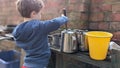 A young boy playing with a mud outdoor kitchen holding stirring a pot