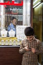 Young boy playing with a smartphone in front of a jewellery store in Isfahan market, while his older father is looking at him