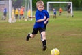 Young boy in blue uniform running to soccer ball on field during game Royalty Free Stock Photo