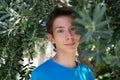 Young boy posing in summer grove among olive trees. Cute smiling happy teen boy 13 years old, looking at camera. Royalty Free Stock Photo