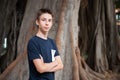 Young boy posing in summer park with ficus trees. Cute spectacled smiling happy teen boy 13 years old, looking at camera Royalty Free Stock Photo