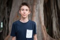 Young boy posing in summer park with ficus trees. Cute spectacled smiling happy teen boy 13 years old, looking at camera