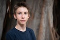 Young boy posing in summer park with ficus trees. Cute spectacled smiling happy teen boy 13 years old, looking at camera Royalty Free Stock Photo