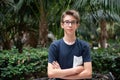 Young boy posing in summer park with palm trees. Cute spectacled smiling happy teen boy 13 years old, looking at camera. Royalty Free Stock Photo