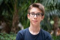 Young boy posing in summer park with palm trees. Cute spectacled smiling happy teen boy 13 years old, looking at camera.