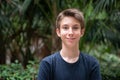 Young boy posing in summer park with palm trees. Cute spectacled smiling happy teen boy 13 years old, looking at camera. Royalty Free Stock Photo