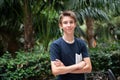 Young boy posing in summer park with palm trees. Cute spectacled smiling happy teen boy 13 years old, looking at camera.