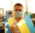 A young boy in a protective mask holds the national flags of Ukraine yellow-blue. Stop coronavirus. Coronavirus pandemic COVID-19