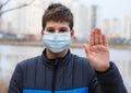 Young boy in protective medical mask on a face looking at camera with hand up, stop sign. Cute teenager outdoor in mask Royalty Free Stock Photo