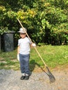 Young boy is raking garbage near his house. Concept of harvesting and autumn renewal. Royalty Free Stock Photo