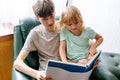 Young Boy Reads a Book to a Little Girl While Sitting on a Green Couch