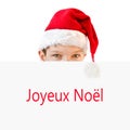 Young boy in red Santa hat hiding behind a paper Joyeux Noel