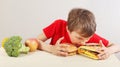 Young boy in red at the table chooses between fastfood and vegetable and fruits