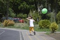 Young boy running with green balloon near tree and grass, wearing shorts Royalty Free Stock Photo