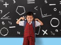 Young boy in school uniform flexing his muscles infront of blackboard