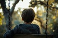 A young boy is seated on a swing in a park setting, A boy sitting alone on a swing, lost in thought