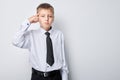 Young boy in shirt and tie making a thinking gesture against a gray background