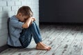 A young boy sits alone with a sad feeling at school near the wall. Offended child abandoned in the corridor and bent against a Royalty Free Stock Photo
