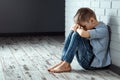 A young boy sits alone with a sad feeling at school near the wall. Offended child abandoned in the corridor and bent against a Royalty Free Stock Photo