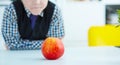 Young boy sits and looks at the red apple at the table. Time for lunch.