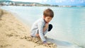 A young boy sits on a sunny beach digging with hands warm sand as he enjoys a fun-filled day of play and exploration Royalty Free Stock Photo