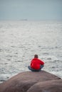 Young Boy Sitting On Coastal Rock Looking At Sea