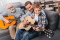 Young boy sitting on couch in living room, playing guitar with his father Royalty Free Stock Photo