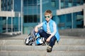 Young boy sitting near grey wall with inline roller skates and all protection at outdoor skate park Royalty Free Stock Photo