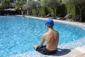 A Young Boy is Sitting Near the Pool. Empty Space for Text. A Boy Sits by the Pool and Prepares to Dive and Swim in the Clear Blue Royalty Free Stock Photo