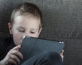 Young boy sitting on sofa in living room and watching cartoons on tablet. Portrait of a smart pre-school child using devices at Royalty Free Stock Photo