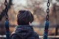 A young boy is sitting on a swing in the park, A boy sitting alone on a swing, lost in thought Royalty Free Stock Photo