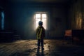 Young boy standing on the floor of a dark, abandoned room.