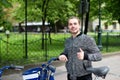 Young boy standing with hired bike near park with green trees.