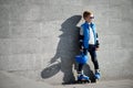 Young boy standing near grey wall with inline roller skates and all protection at outdoor skate park Royalty Free Stock Photo