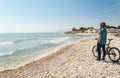 Young boy standing next to a bike on a pebble beach looking at a pirate castle.