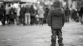 A young boy stands on tiptoes trying to get a glimpse of the event happening in the square back to the camera as strains