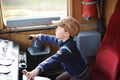 A young boy steering a locomotive and train in a driving compartment or cabin with handles and meters as a train driver