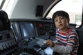 A young boy steering a locomotive and train in a driving compartment or cabin with handles and meters as a train driver