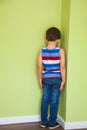 Boy in a striped t-shirt stands in the corner with his face turned away because he has been punished