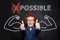 Young boy student with text possible holding thumbs up on blackboard background. Success and develop concept