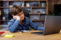 Young boy studying remotely at home using laptop. Tired schoolboy falling asleep during an online lesson with teacher Royalty Free Stock Photo