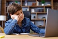 Young boy studying remotely at home using laptop. Tired schoolboy falling asleep during an online lesson with teacher Royalty Free Stock Photo