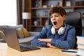 Young boy studying remotely at home using laptop. Tired schoolboy yawning during an online lesson with teacher. Distance Royalty Free Stock Photo