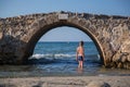 Young boy in swimsuit stands under an old stone bridge in water of sea, in Greece Royalty Free Stock Photo