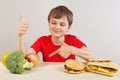 Young boy at the table chooses between fastfood and healthy diet on white background Royalty Free Stock Photo