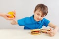 Young boy at the table chooses between fastfood and orange on white background