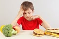 Young boy at the table chooses between fastfood and vegetable and fruits